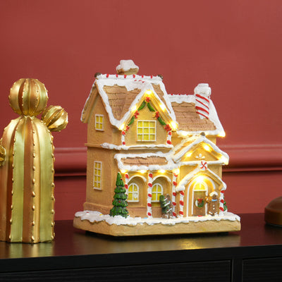 Gingerbread house glowing on a dark shelf against a red wall beside a gold cactus ornament