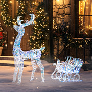 Lit reindeer and sleigh on snow outside a house with fairy lights