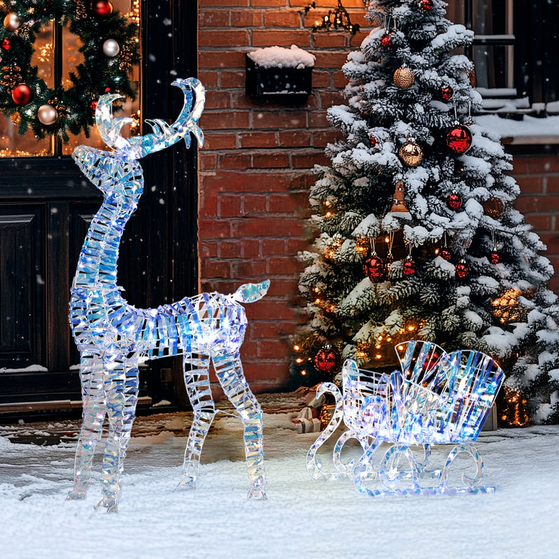 Lit reindeer and sleigh in a snowy yard outside a door with a wreath
