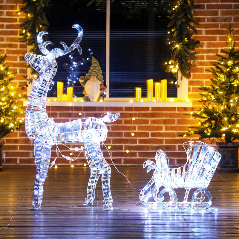 Glowing reindeer and sleigh on a decking floor with candles in the window behind