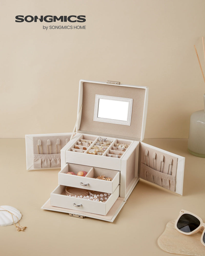 White jewellery box open on a beige dressing table beside sunglasses, filled with rings and beads
