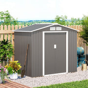Warm grey shed beside a picket fence with plants and a watering can