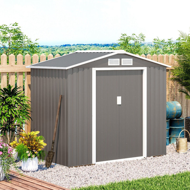 Warm grey shed beside a picket fence with plants and a watering can