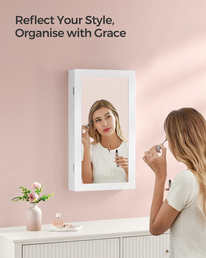 Woman applying make-up in the mirror of the white jewellery cabinet hung above a dresser