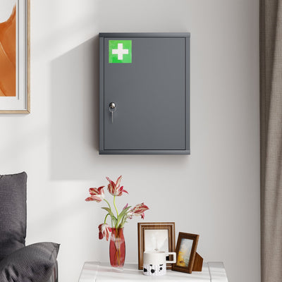 Closed smoke grey medicine cabinet with a green first aid cross mounted on a wall above a table with photo frames and a vase