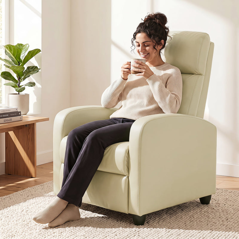 Woman sitting upright in the cream white recliner armchair drinking coffee