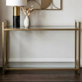 Matte gold console table with clear glass top styled with decorative items against a white hallway wall