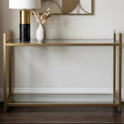 Matte gold console table with clear glass top styled with decorative items against a white hallway wall