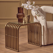 Matte gold slatted end table with clear glass top styled beside a sofa in a living room