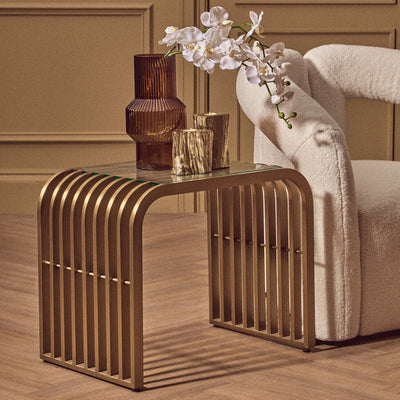 Matte gold slatted end table with clear glass top styled beside a sofa in a living room