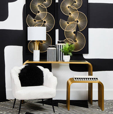 Gold and glass end table in a styled living room setting with lamp and books