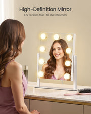 Woman smiling into the compact lit vanity mirror on a dressing table