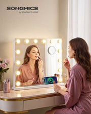 Woman applying lip gloss in the lit vanity mirror on a dressing table with a phone charging