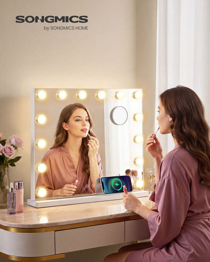 Woman applying lip gloss in the lit vanity mirror on a dressing table with a phone charging