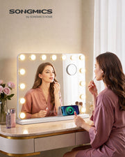 Woman applying lip gloss in the lit vanity mirror on a dressing table with a phone charging