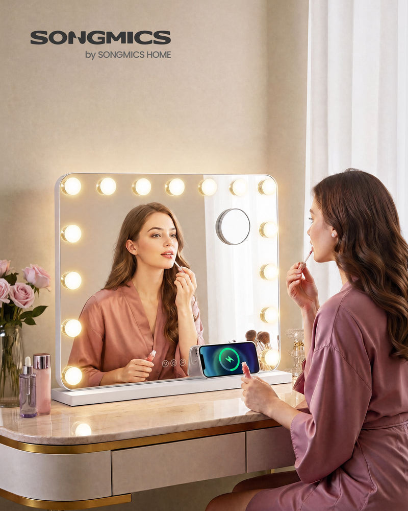 Woman applying lip gloss in the lit vanity mirror on a dressing table with a phone charging