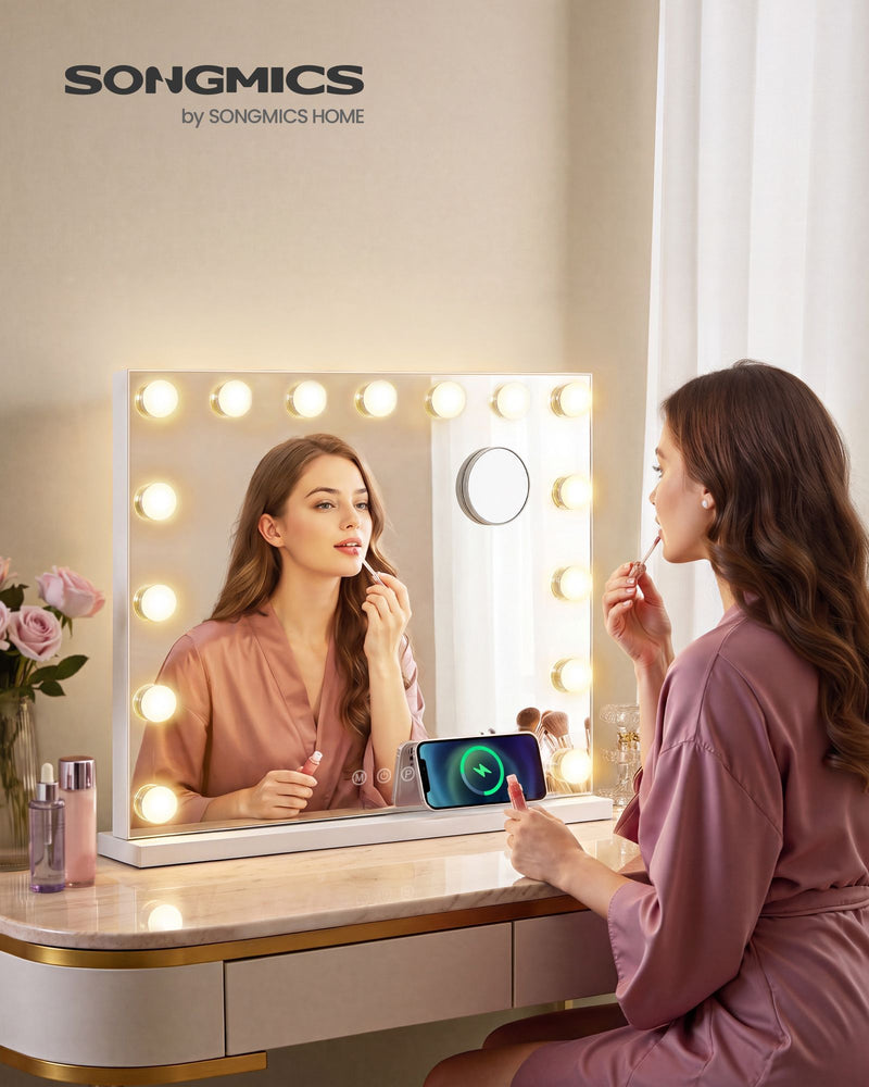Woman applying lip gloss in the lit vanity mirror on a dressing table with a phone charging