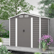 Light grey 7x4ft metal shed with white corner trims on a paved patio next to garden planting
