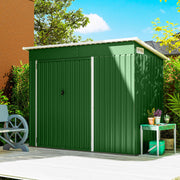 Green metal garden shed standing closed on a patio beside a house wall