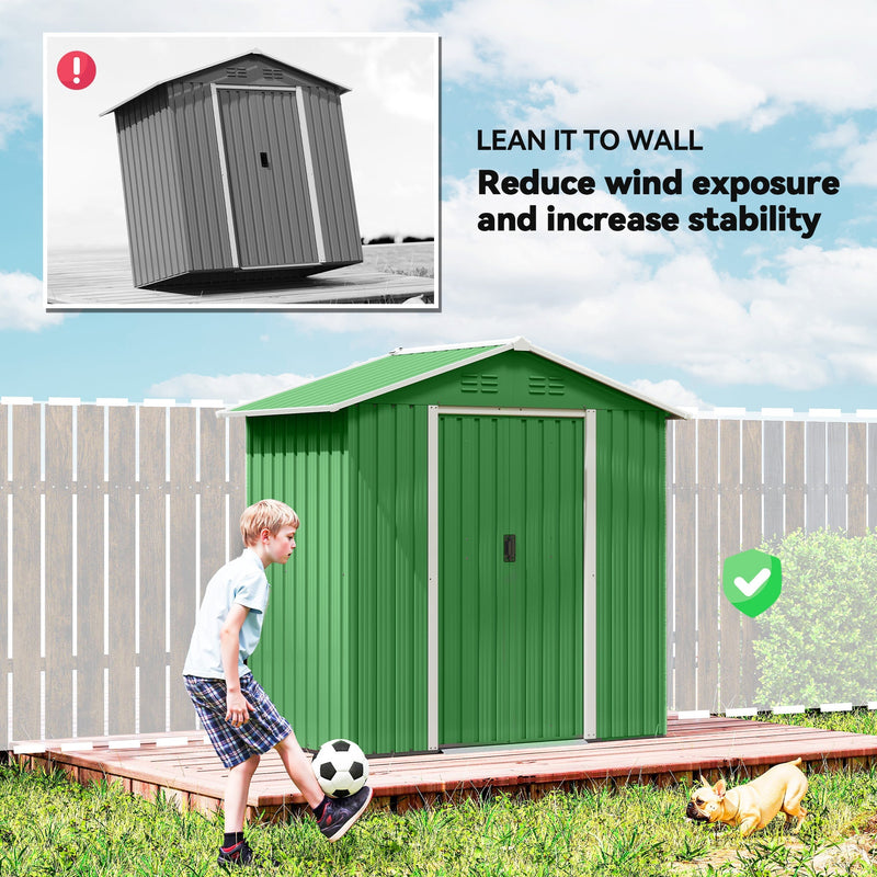 Green metal shed standing against a fence to reduce wind exposure in a garden