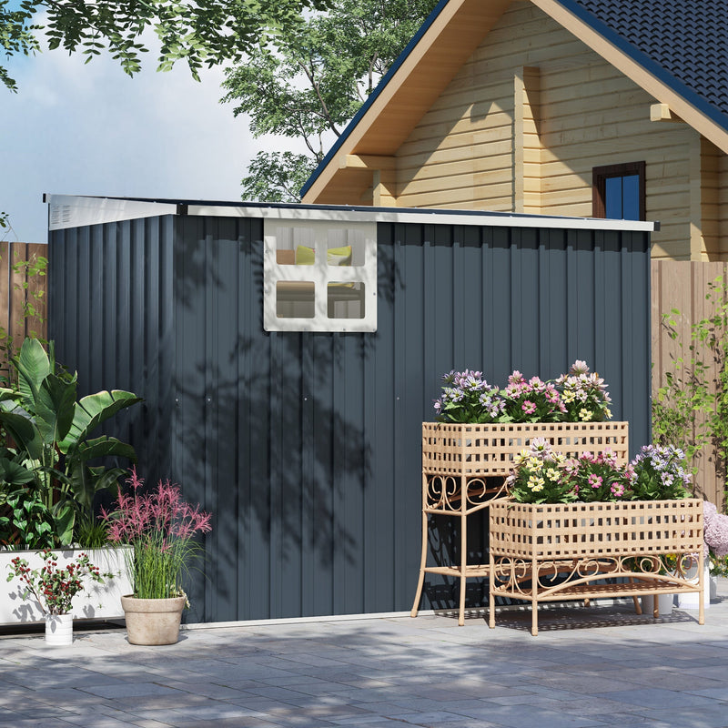 Long side of the dark grey shed with its window, beside a cabin and planters