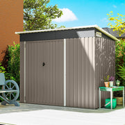 Light grey metal garden shed standing closed on a patio beside a house wall