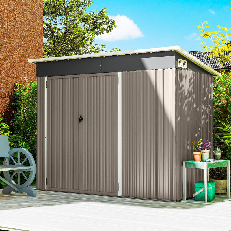 Light grey metal garden shed standing closed on a patio beside a house wall