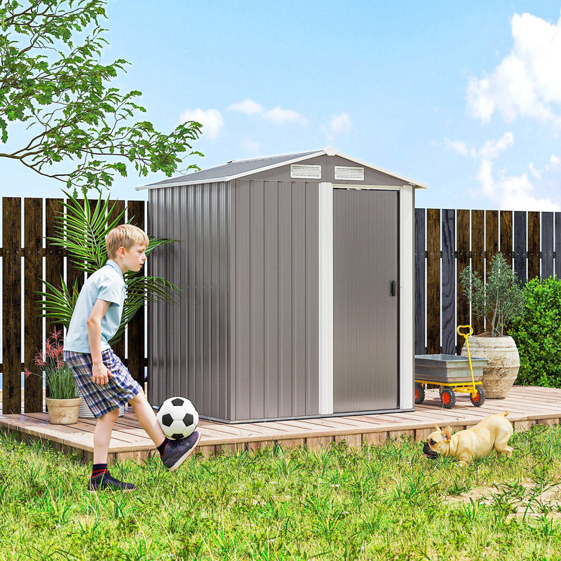 Grey apex shed on grass beside a wooden fence with a child and a dog in the garden