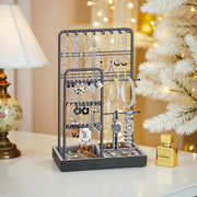 Black metal jewellery stand displaying silver necklaces, earrings and a watch on a bedside table