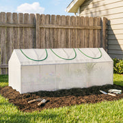 White greenhouse with arched window frames on dark soil in front of a wooden fence
