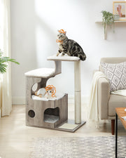 Cat tree in a living room with a tabby cat on top and a kitten in the cave