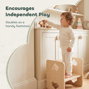 Toddler standing on the chair used as a footstool beside a cabinet
