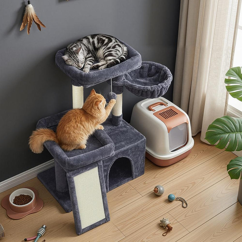 Lifestyle photo of two cats using the tree beside a litter box in a living room corner