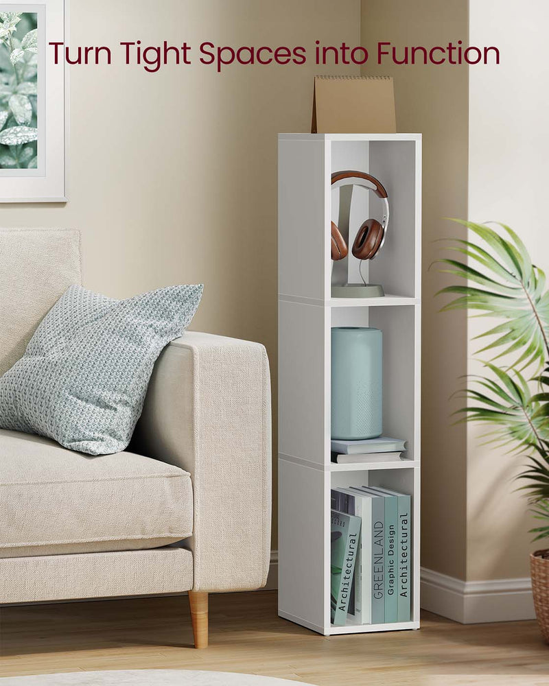 Narrow white cube bookcase holding headphones, a speaker and books beside a sofa