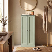 Light green bathroom cabinet used as hallway storage beside a console table and coat stand