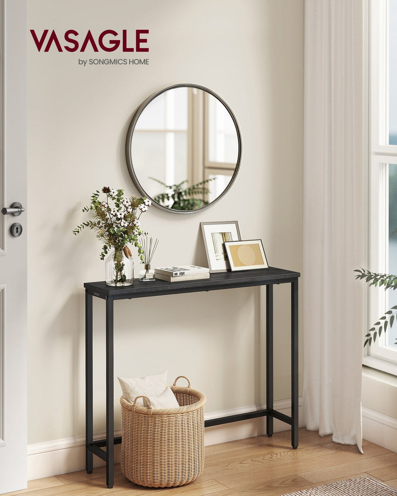 Black narrow console table in a hallway beneath a round mirror with a woven basket underneath