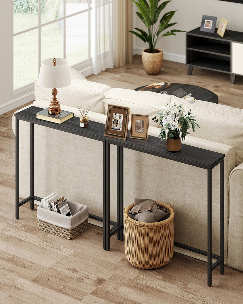 Two black narrow console tables placed end to end behind a sofa in a living room