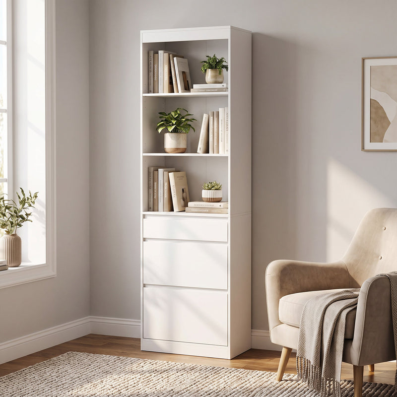 White bookcase with 3 open shelves and 3 drawers styled with books and plants next to an armchair