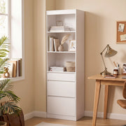 White narrow bookcase with 3 drawers in a warm study corner next to a wooden desk and lamp