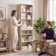 Oak wood effect bookcase placed in a living room beside a sofa and armchair