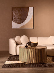 Round bamboo coffee table on a textured rug beside a neutral linen sofa