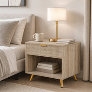 Natural wood bedside table styled beside a bed with lamp, books and mug