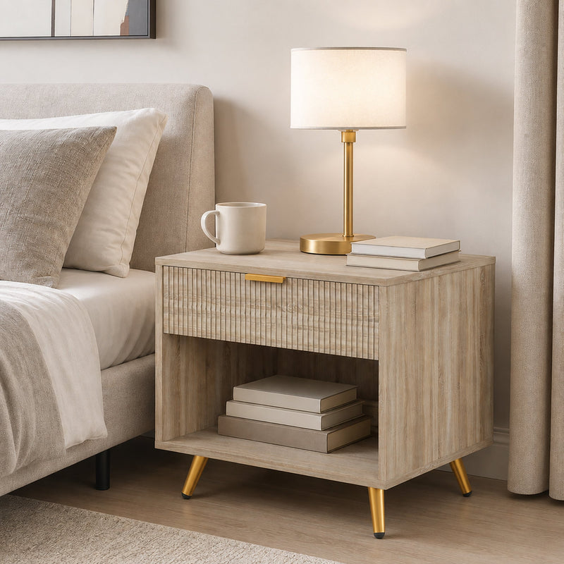 Natural wood bedside table styled beside a bed with lamp, books and mug