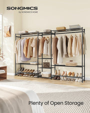 Black open wardrobe unit installed in a real bedroom beside the bed, holding folded clothes, shoes, and a handbag on its open shelves.