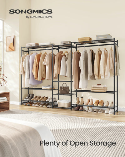 Black open wardrobe unit installed in a real bedroom beside the bed, holding folded clothes, shoes, and a handbag on its open shelves.