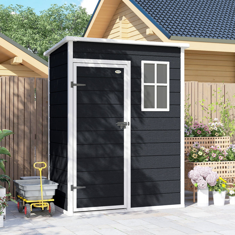 The black plastic shed standing against a wooden fence beside a house with a garden cart