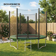 Dark green trampoline on a lawn beside a wooden fence with footballs and a picnic basket