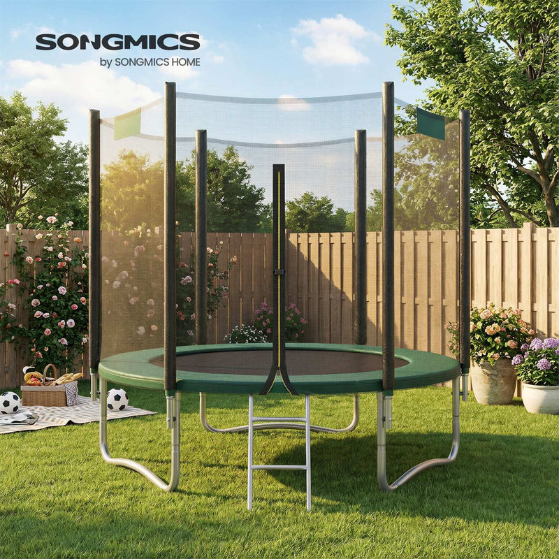 Dark green trampoline on a lawn beside a wooden fence with footballs and a picnic basket