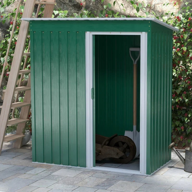 Green shed on a patio with the sliding door open showing a wheelbarrow and spade inside