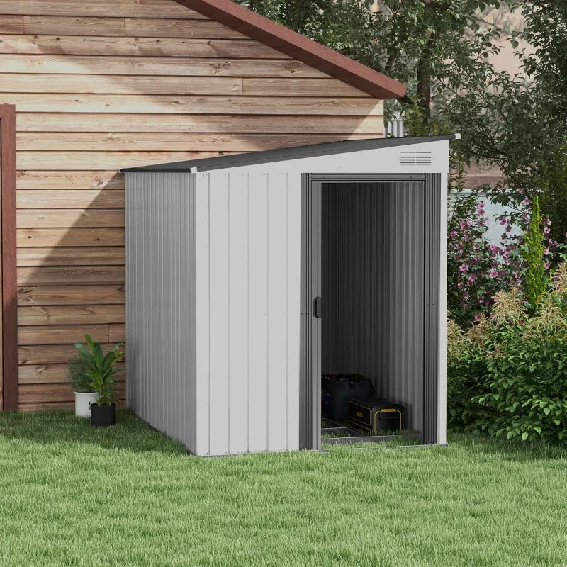 The shed on a lawn against a timber-clad house wall, door open with tools stored inside